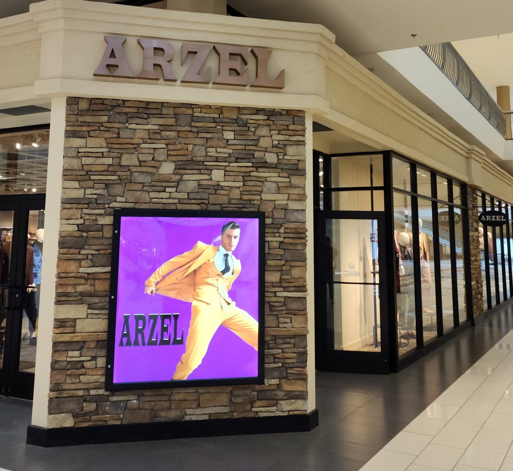 An ARZEL boutique storefront in a shopping mall, featuring a stone-textured facade, a large digital display screen showing a model, and the brand name 'ARZEL' above the entrance.