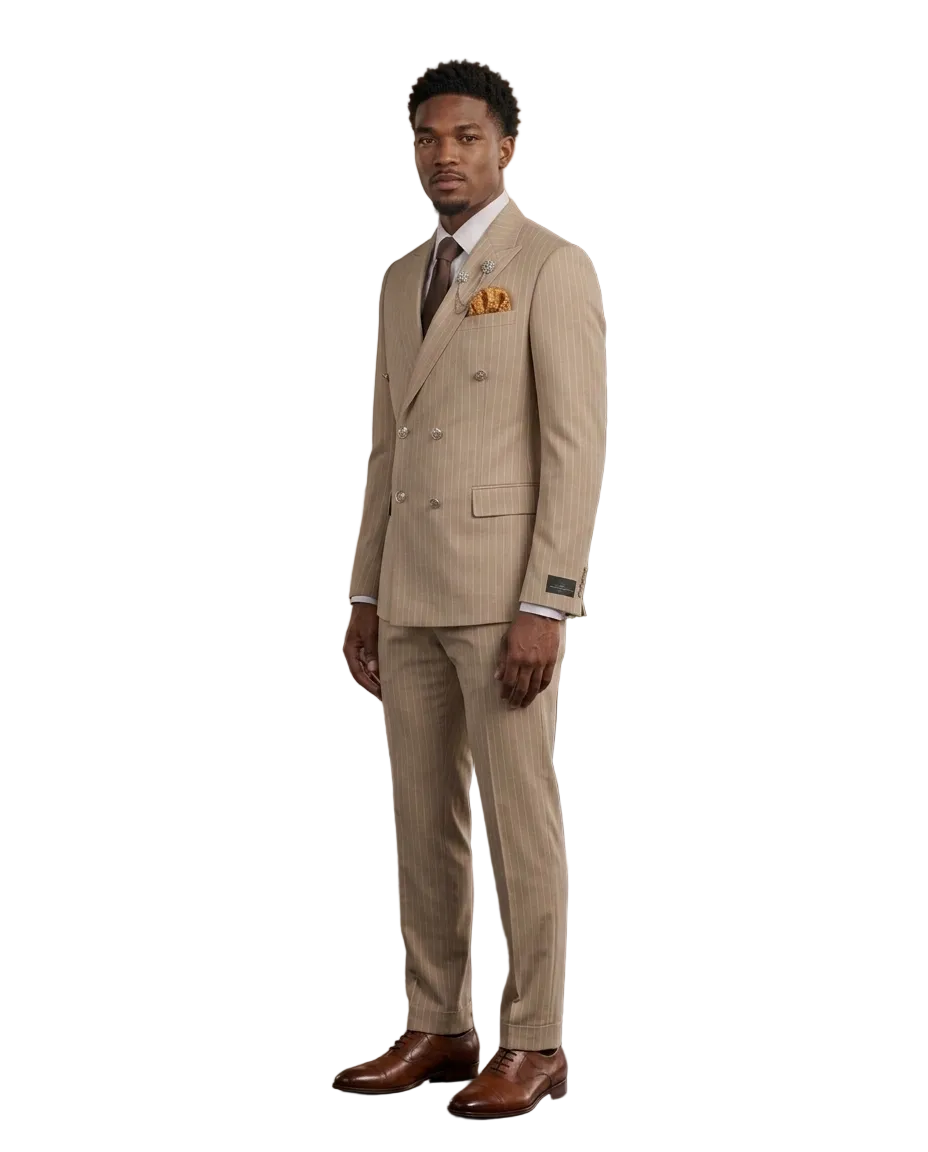 A man wearing a beige double-breasted pinstripe suit with a white shirt, brown tie, and brown leather dress shoes, standing in a modern loft-style room with wood paneling, brick walls, and leather chairs.